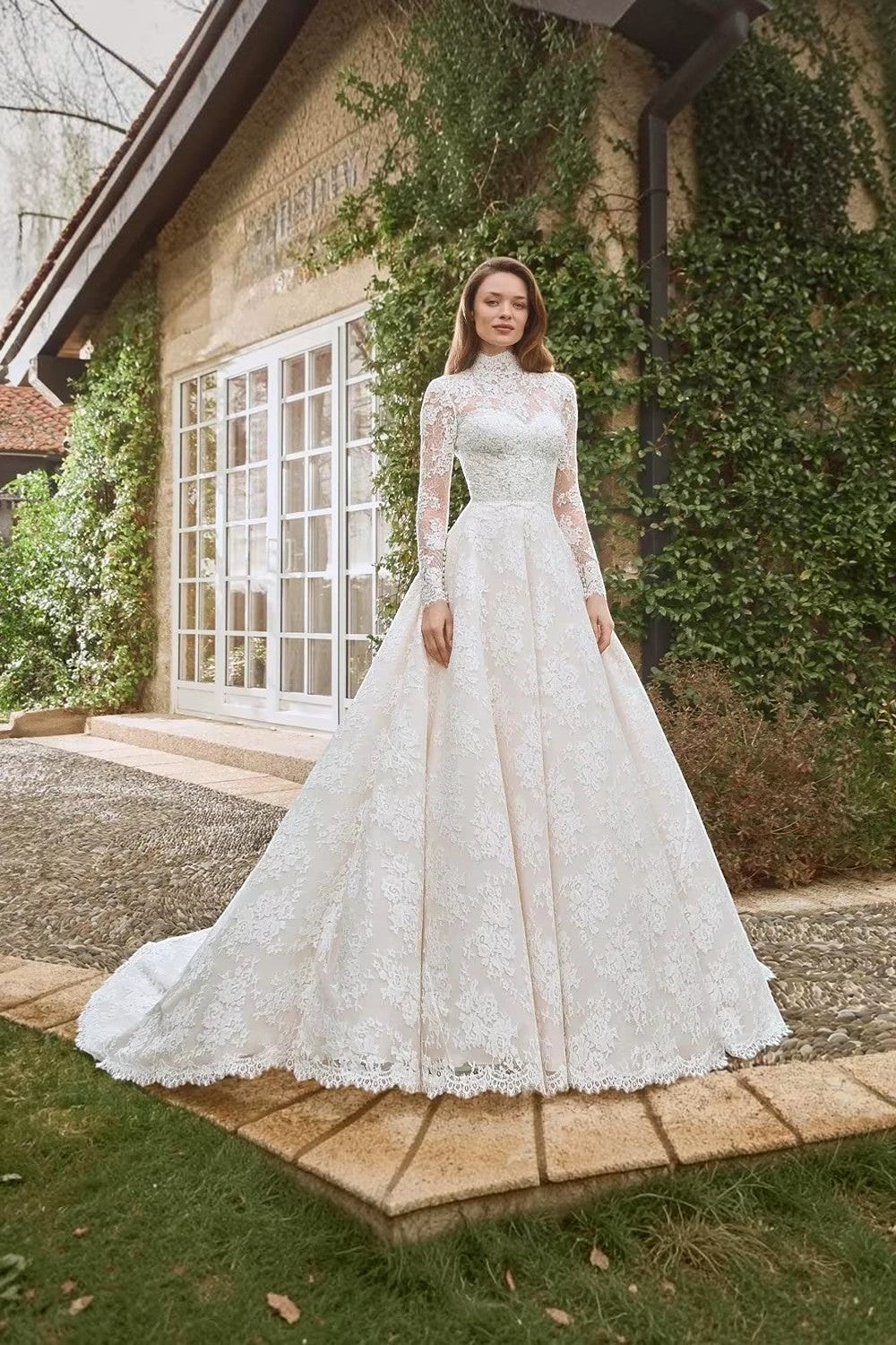 TheBlissWedding white A-line wedding dress with high neck, long lace sleeves, and intricate floral appliques outdoors.
