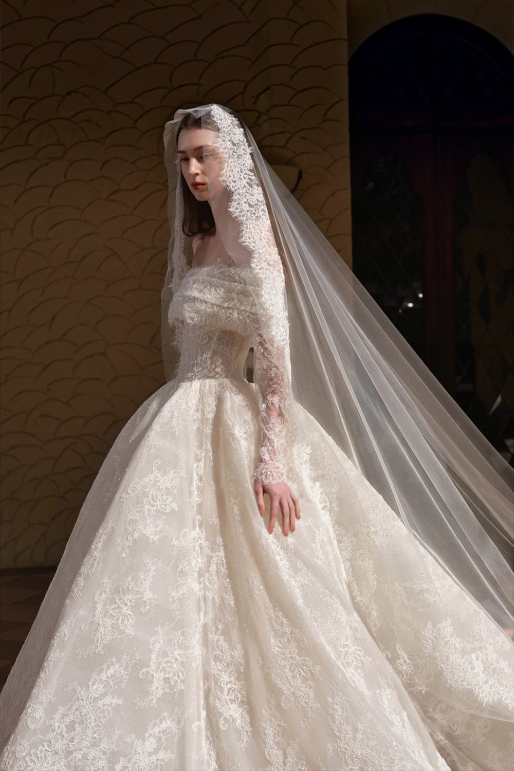 TheBlissWedding white boho A-line wedding dress with off-shoulder neckline, long lace sleeves, and a long veil.