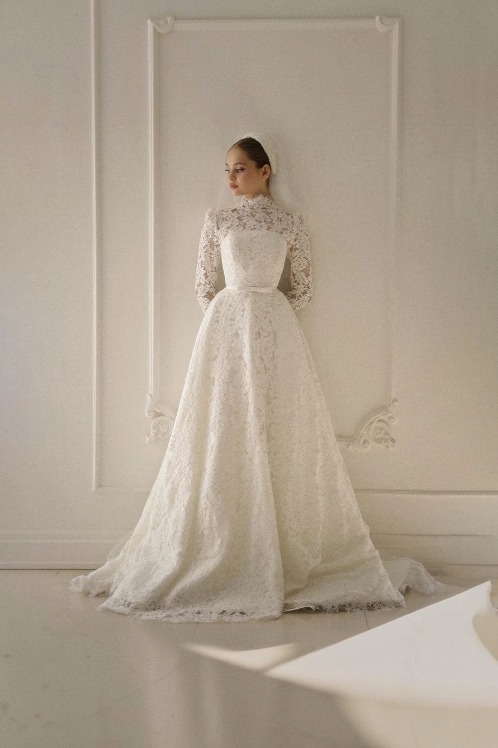TheBlissWedding modest A-line bridal gown with high neck, long lace sleeves, and a sweep train in ivory lace.