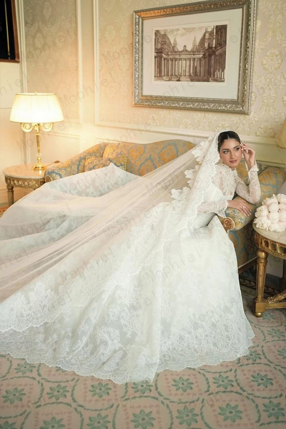 TheBlissWedding white lace A-line wedding dress with long sleeves and a long veil, worn by a bride on a vintage sofa.