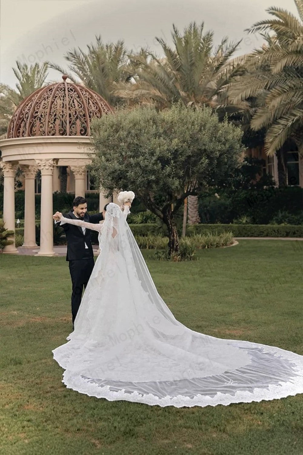 TheBlissWedding white lace A-line wedding dress with long sleeves and a long sweep train worn by a bride in a garden