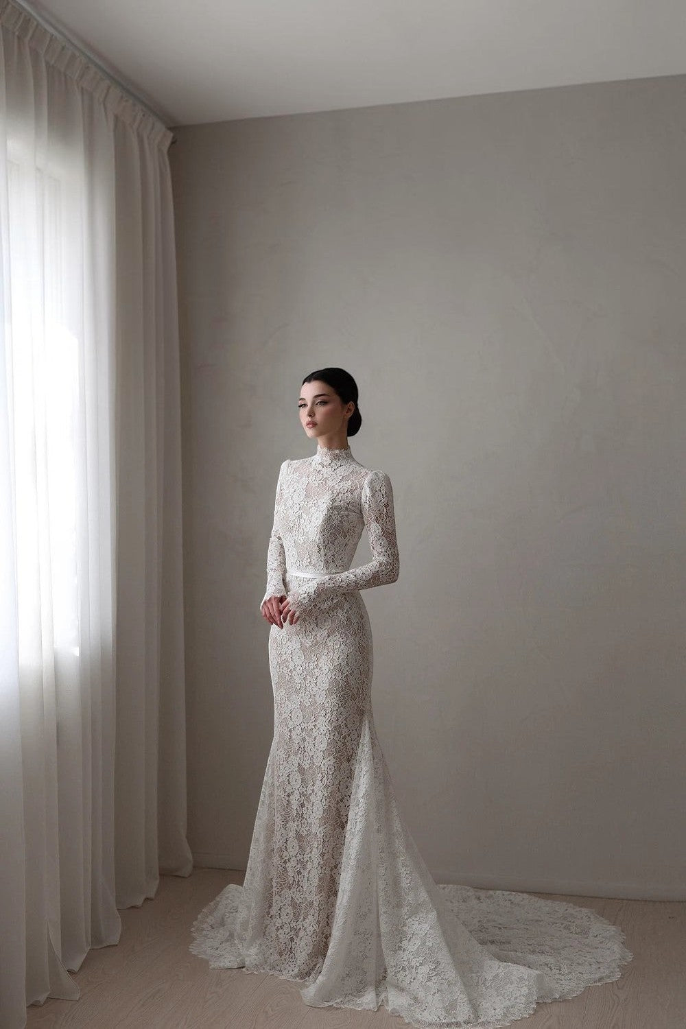 TheBlissWedding mermaid bridal gown with high neck, long lace sleeves, and a sweep train in a minimalist room.