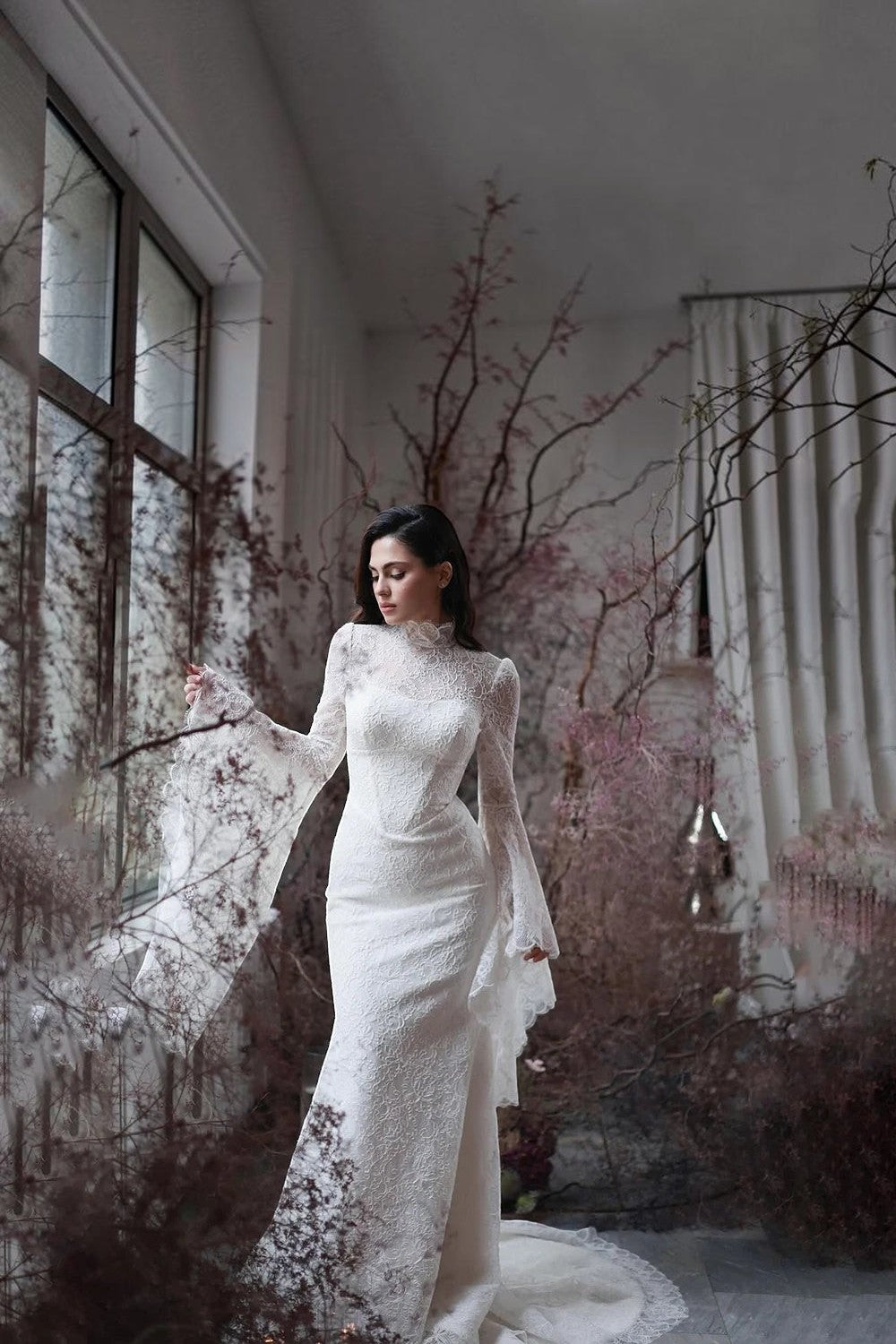 TheBlissWedding white lace mermaid wedding dress with high neck and long flare sleeves in a rustic indoor setting