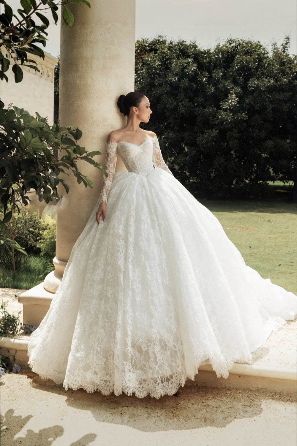 TheBlissWedding off-shoulder lace A-line wedding dress with long sleeves and a dramatic train in a garden setting.