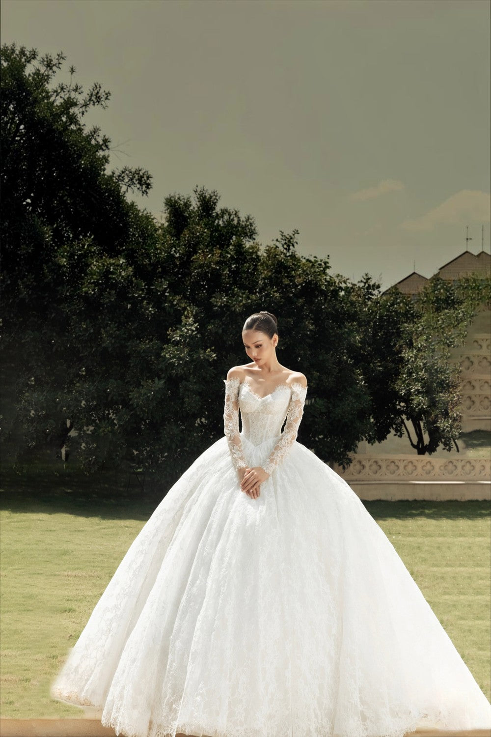 TheBlissWedding off-shoulder lace wedding dress with long sleeves and a voluminous A-line skirt in a garden setting.
