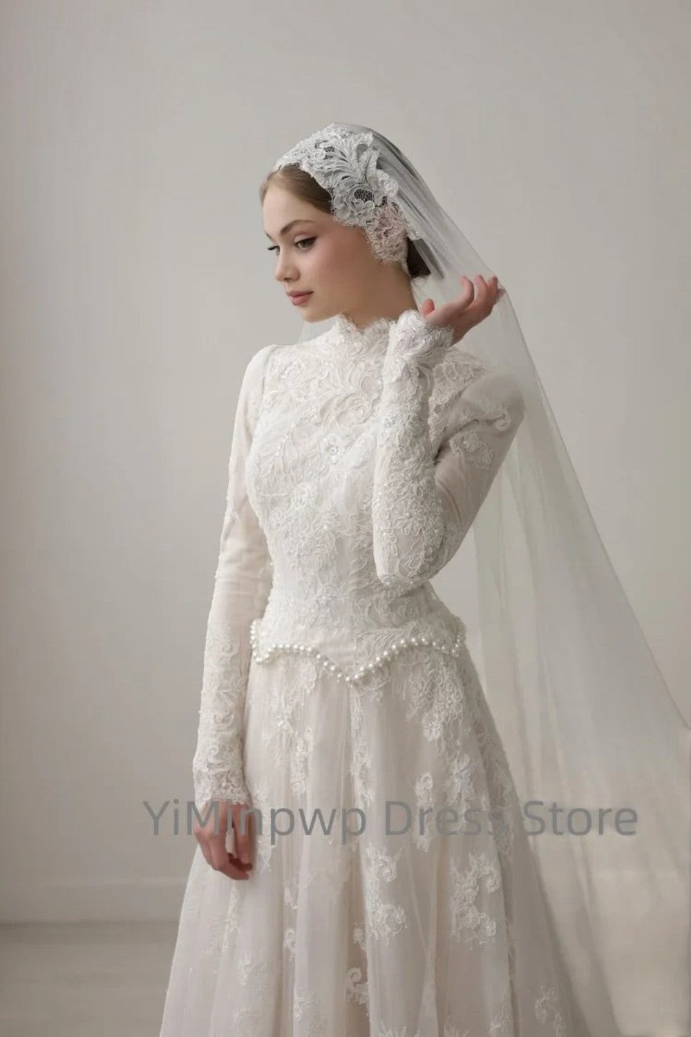TheBlissWedding white modest wedding dress with high collar, long lace sleeves, and pearl-accented waistline.