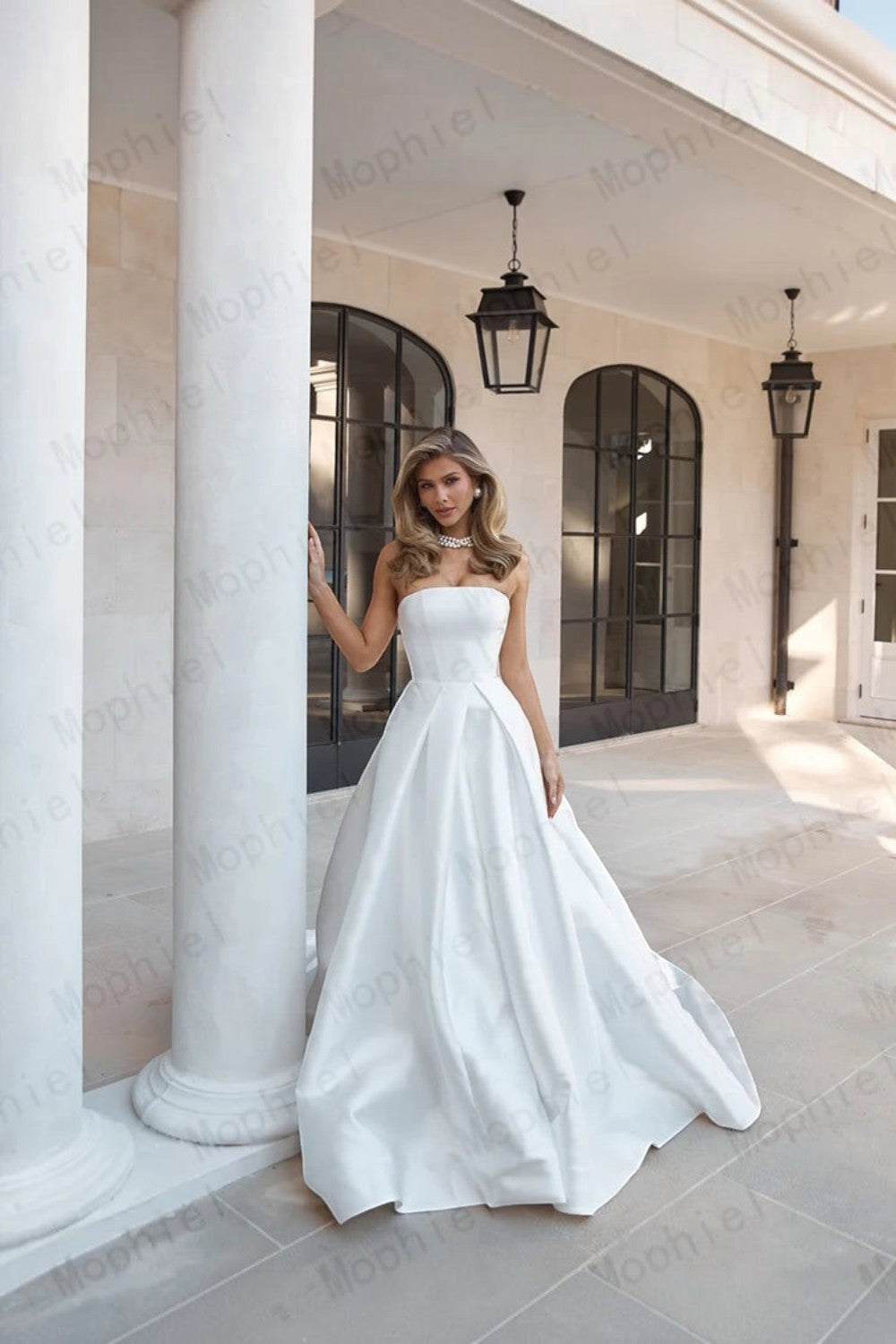 TheBlissWedding strapless white satin A-line wedding dress with a sweep train, worn by a model in a stone courtyard.