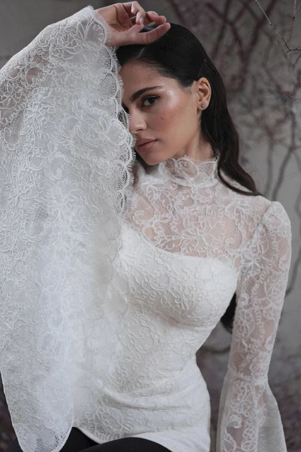TheBlissWedding white lace boho wedding dress featuring a high neck and dramatic long flare sleeves on a model.