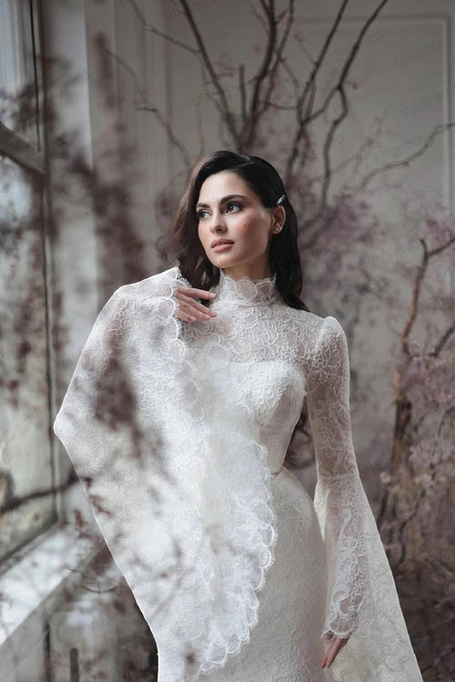 TheBlissWedding white boho mermaid wedding dress with high neck, intricate lace, and dramatic long flare sleeves.